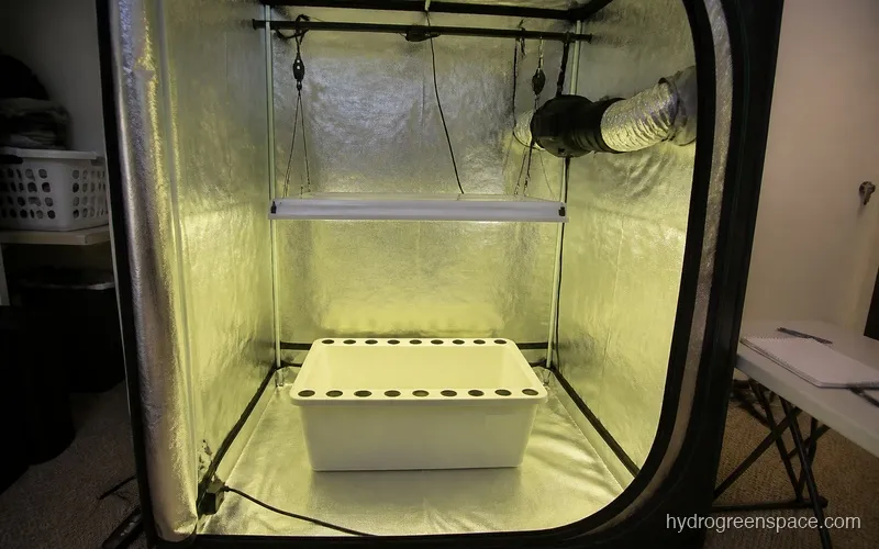 Grow tent interior showing light hanging from top, inline fan ducted through vent port, and empty hydroponic system on the floor before reservoir fill